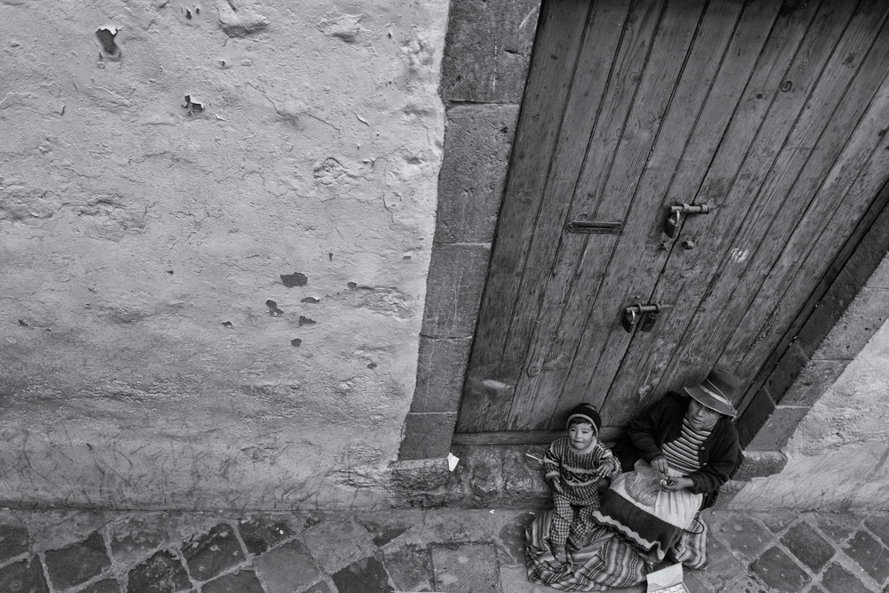 Mother & son sitting outside a house. son waving to people. mother knitting while waiting for the bus.