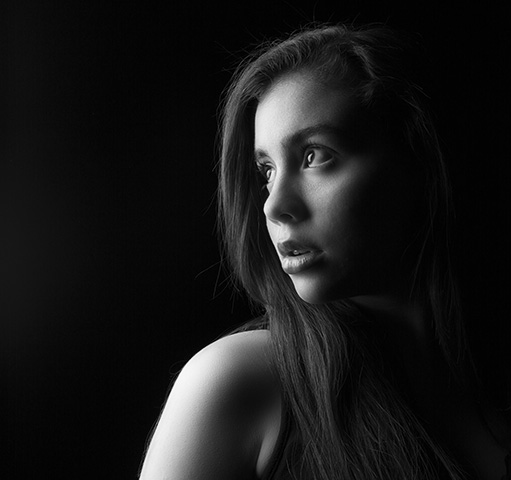 black and white portrait in studio lighting of young girl. Black and white portrait. Low key portrait. Minimalist studio lighting setup.