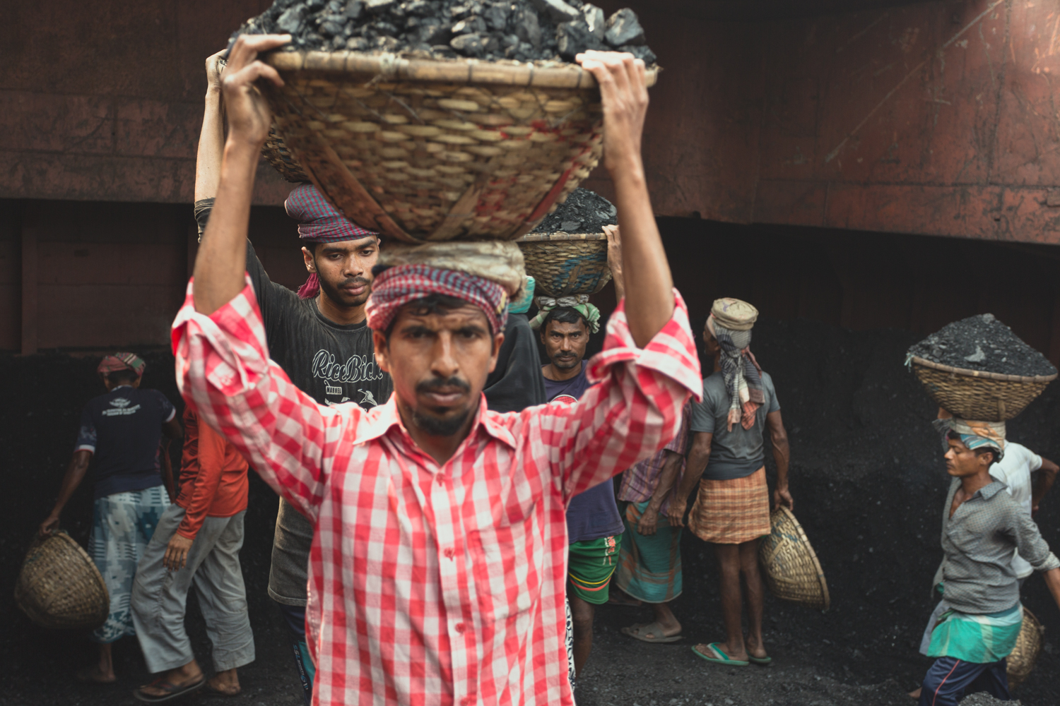 Heavy baskets of coal are transported on the workers' heads in hot conditions at Dhaka, Bangladesh.