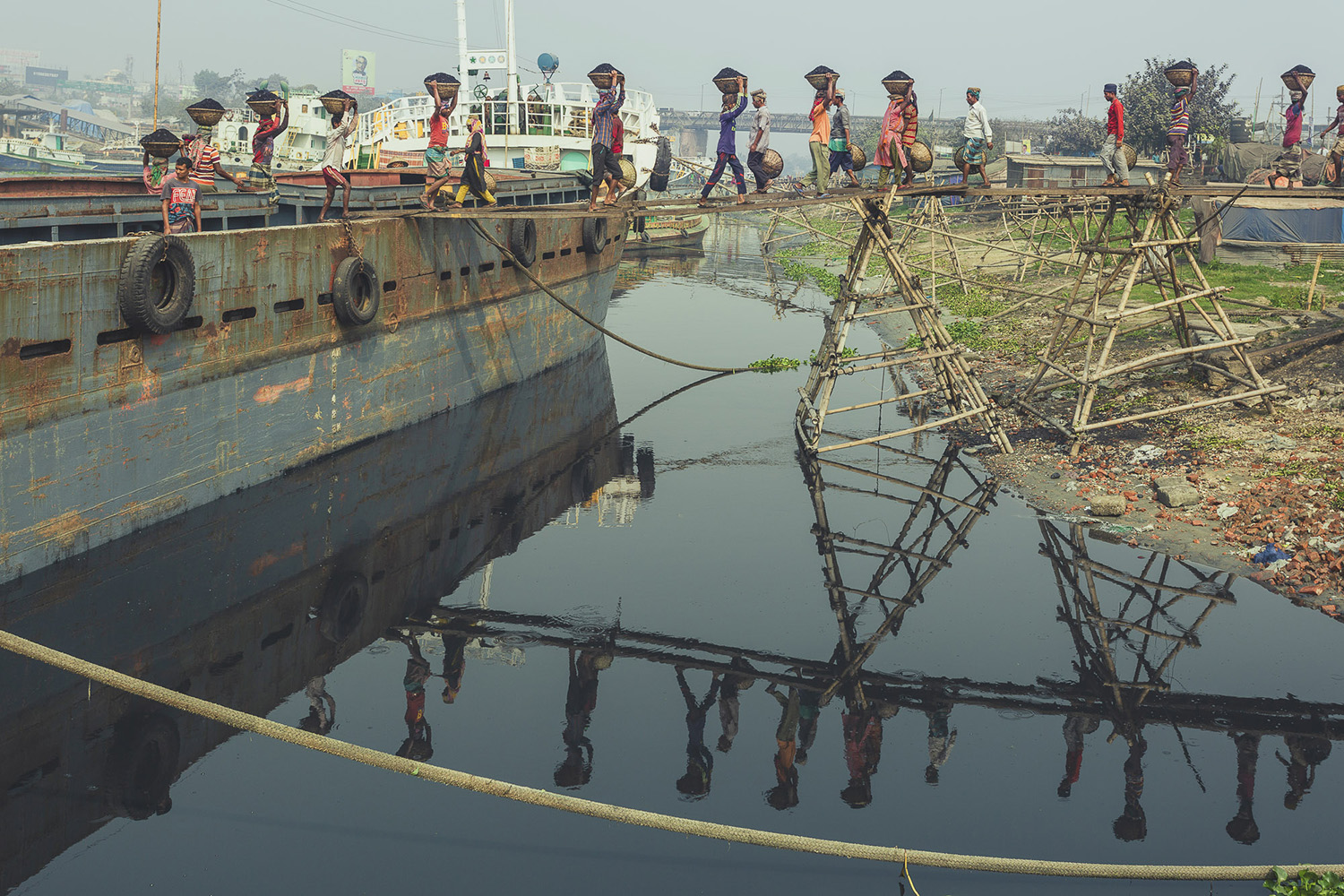 Coal workers in Dhaka, Bangladesh transporting baskets of coal across the bridge.