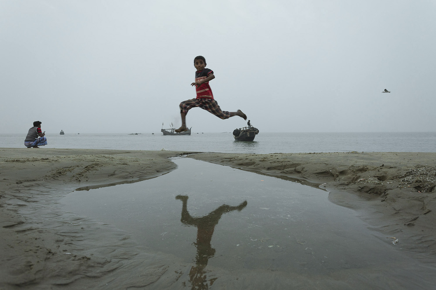 A child leaping over puddles in the sand at  Bay of Bengal, Cox’s Bazar Bangladesh