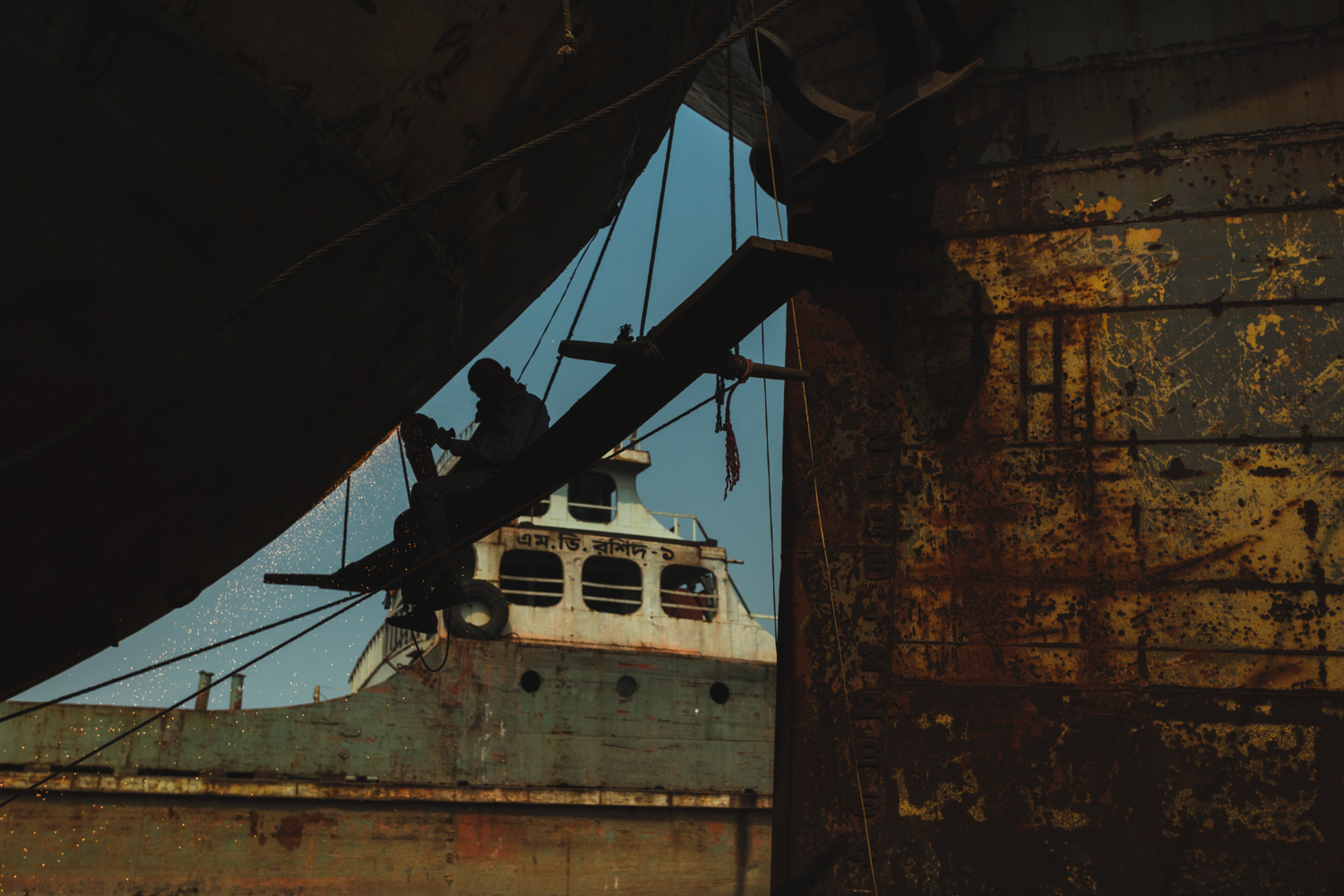 Worker on light platform to access the side of the ship at Dhaka, Bangladesh Shipyard.